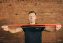 Man stretching a resistance band in front of a brick wall.