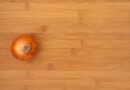 an aerial view of a bamboo cutting board with a whole, unpeeled onion sitting on top of it.