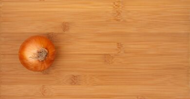 an aerial view of a bamboo cutting board with a whole, unpeeled onion sitting on top of it.