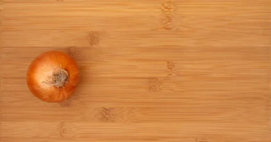 an aerial view of a bamboo cutting board with a whole, unpeeled onion sitting on top of it.