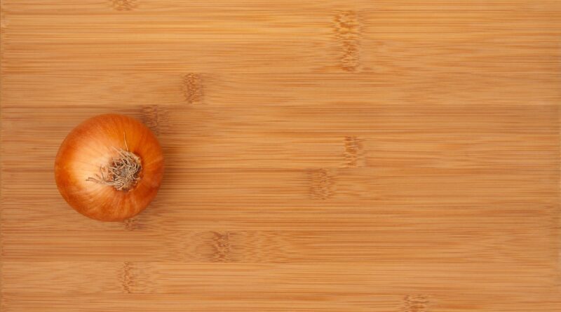 an aerial view of a bamboo cutting board with a whole, unpeeled onion sitting on top of it.