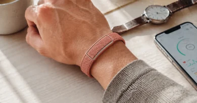 Minimalist screenless fitness tracker worn on a wrist beside an analog watch and smartphone, representing the rumored Google Fitbit Air.